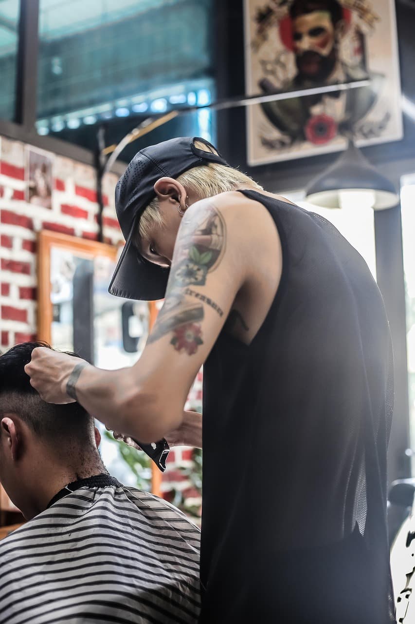 Barber in a cap taking the clippers to a customer in a striped cape